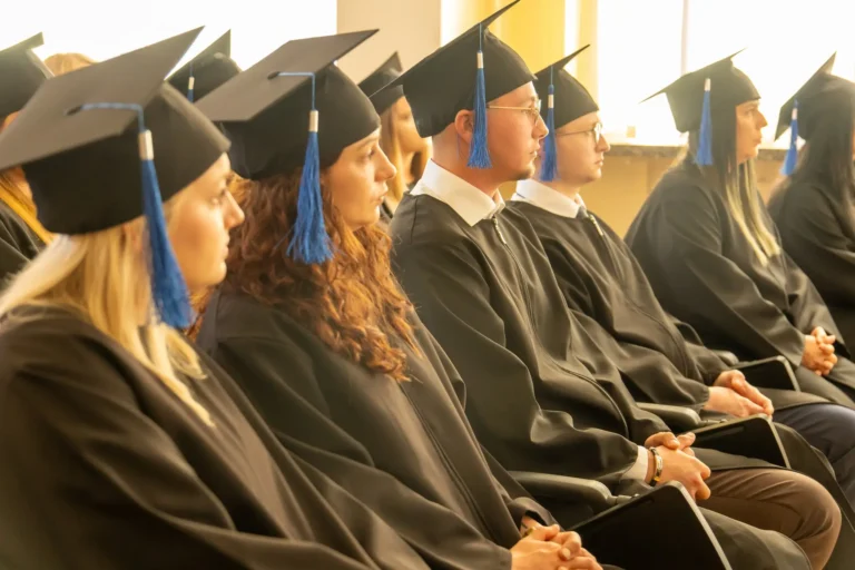 Na zdjęciu widoczni są studenci w strojach akademickich, w tym biretach, siedzący na dyplomatorium.