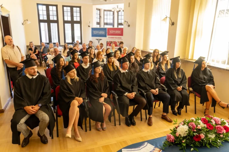 Na zdjęciu widać studentów fizjoterapii w togach akademickich, siedzących na krzesłach w sali podczas uroczystości dyplomowania.